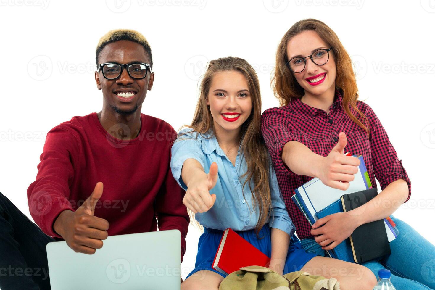 tre contento giovane adolescente studenti con pollici su isolato su bianca foto