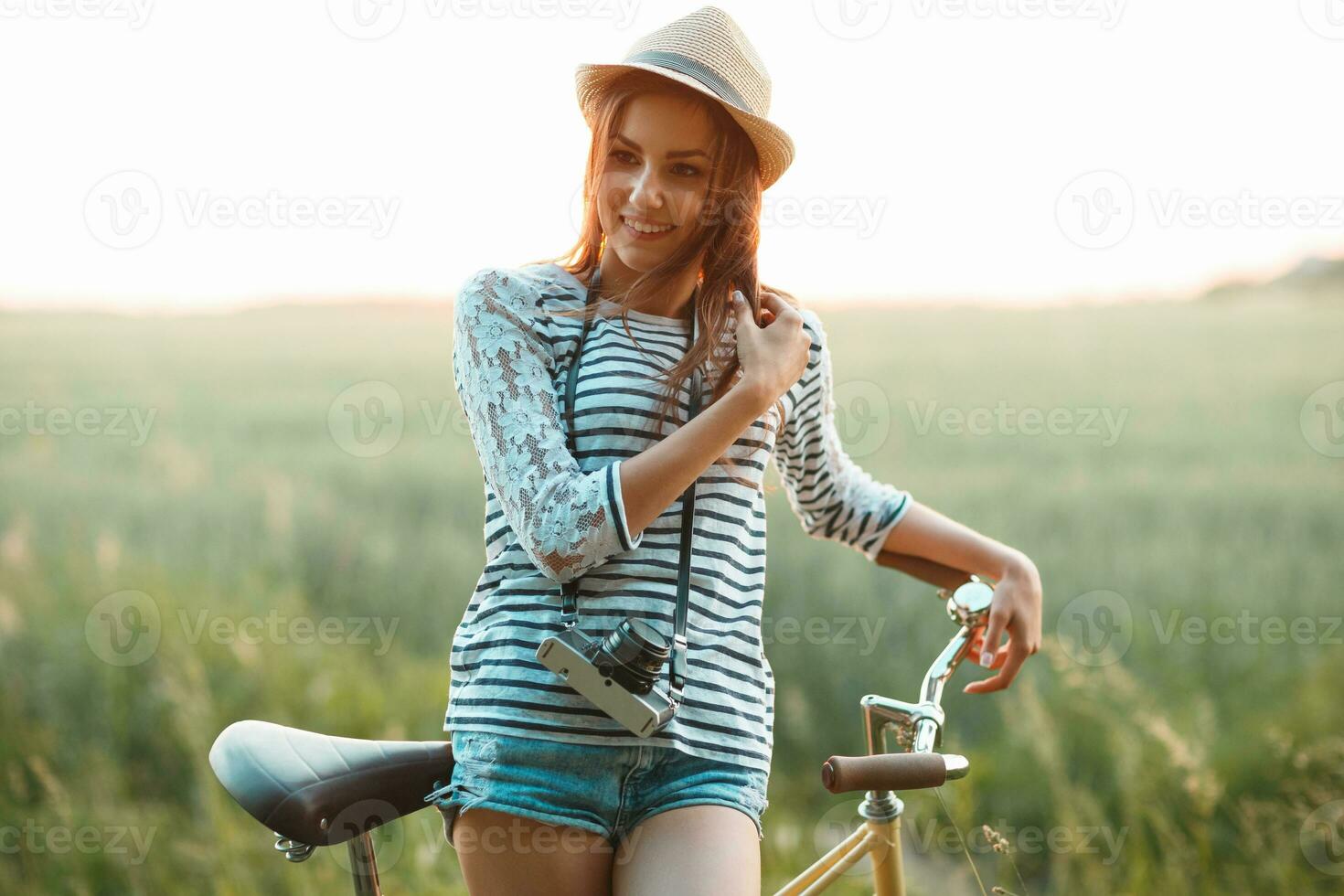 bello giovane donna sta nel un' campo con sua bicicletta foto