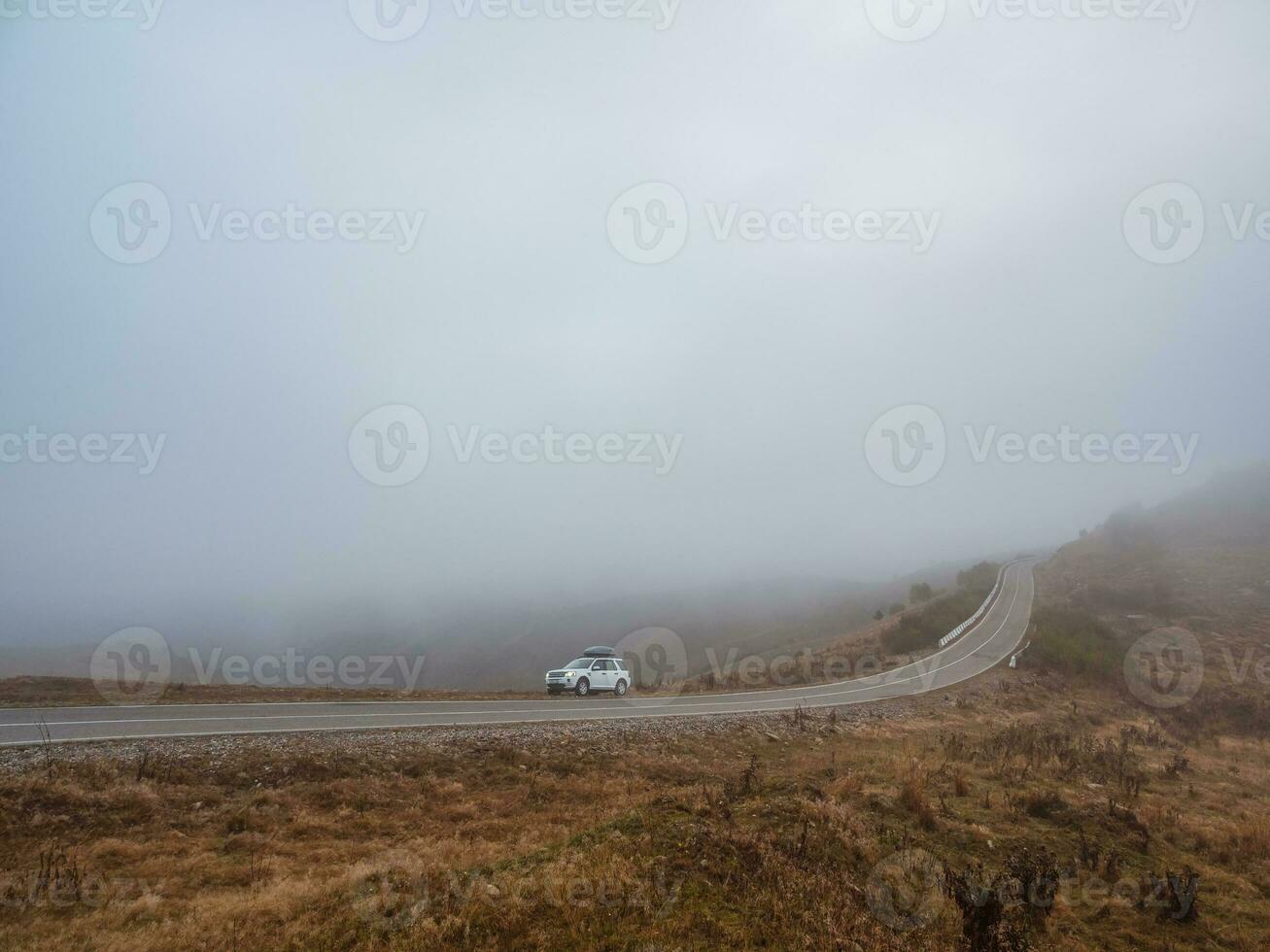 mattina montagna autostrada nel denso nebbia. bianca auto suv con nebbia li foto