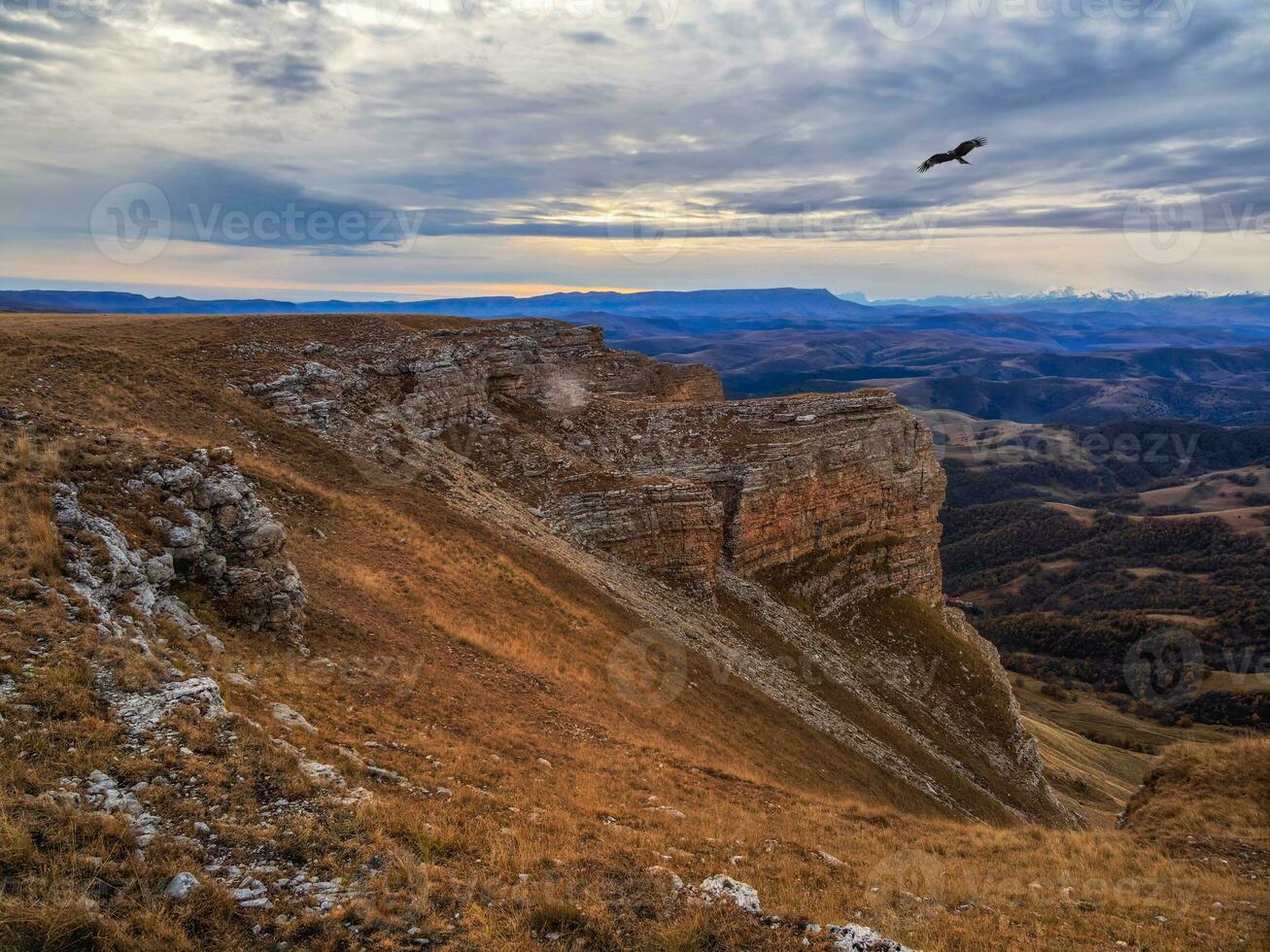 mattina autunno paesaggio con colline su alto altopiano e montagna gamma sotto drammatico nuvoloso cielo. il aquila si libra al di sopra di il scogliera. vivido presto mattina autunno colori nel montagne. foto