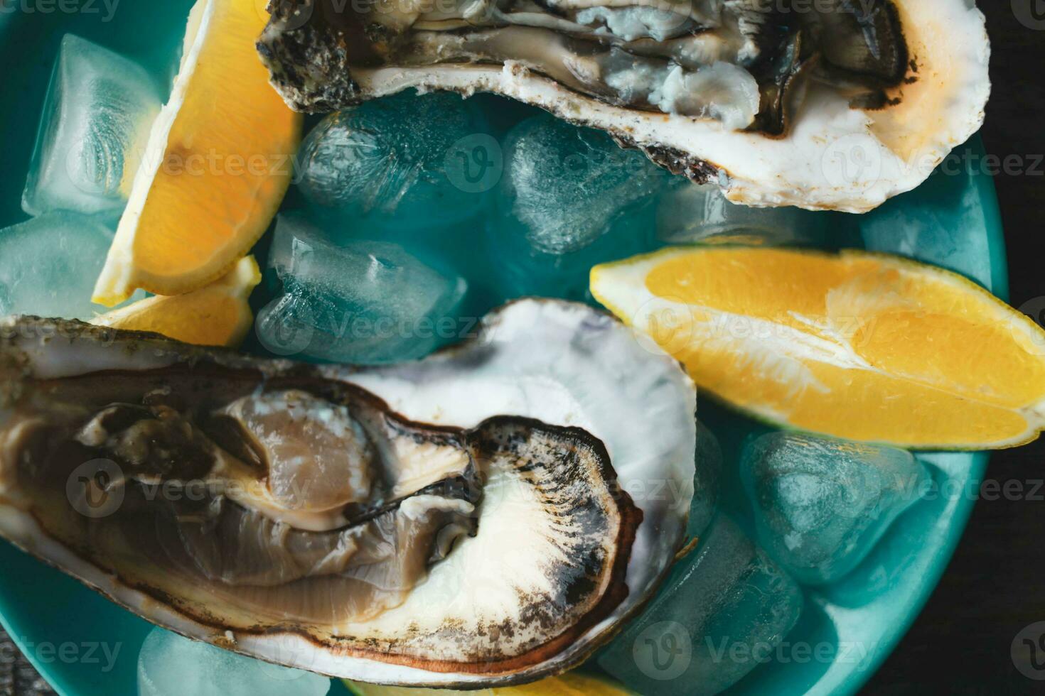 avvicinamento di fresco Aperto crudo Ostriche su un' blu piatto, con Limone e Ghiaccio. salutare frutti di mare. Visualizza a partire dal sopra. frutti di mare. buongustaio cibo. superiore Visualizza. foto