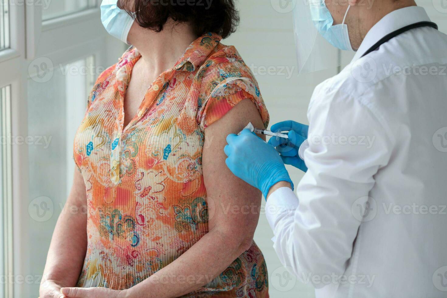 un' maschio medico nel gomma da cancellare guanti detiene un' siringa e dà un iniezione per un più vecchio paziente indossare un' medico maschera. covid-19 o coronavirus vaccino foto