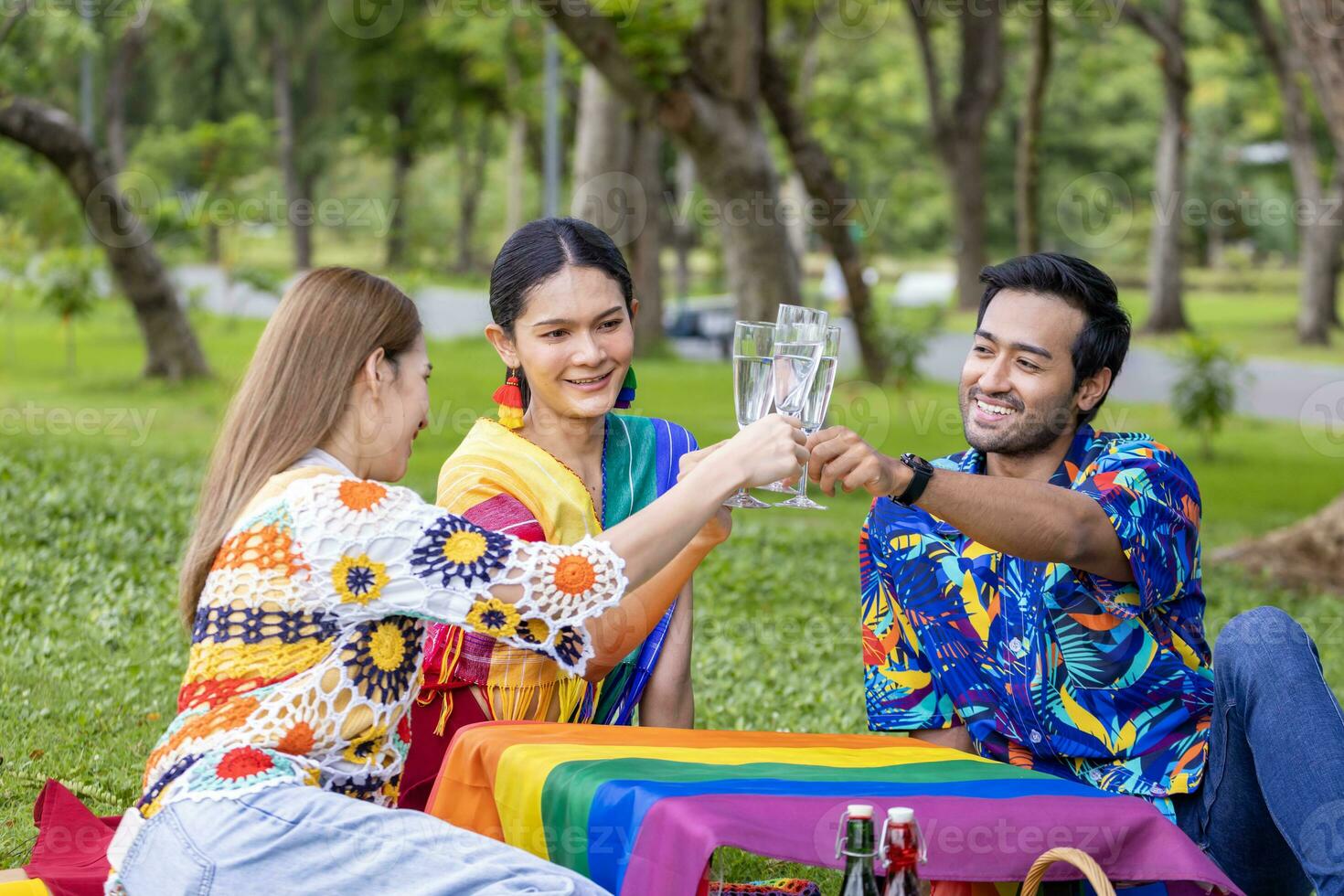 gruppo di persone transgender e omosessuali applaude e celebra il mese dell'orgoglio lgbtq in abiti colorati e bandiera arcobaleno mentre fa un picnic nel parco foto