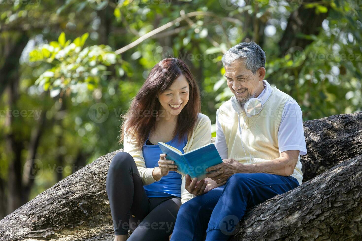 asiatico anziano padre e figlia seduta e lettura un' libro insieme su il ramo di maturo albero durante estate per fisico e mentale Salute e longevità utilizzo. foto