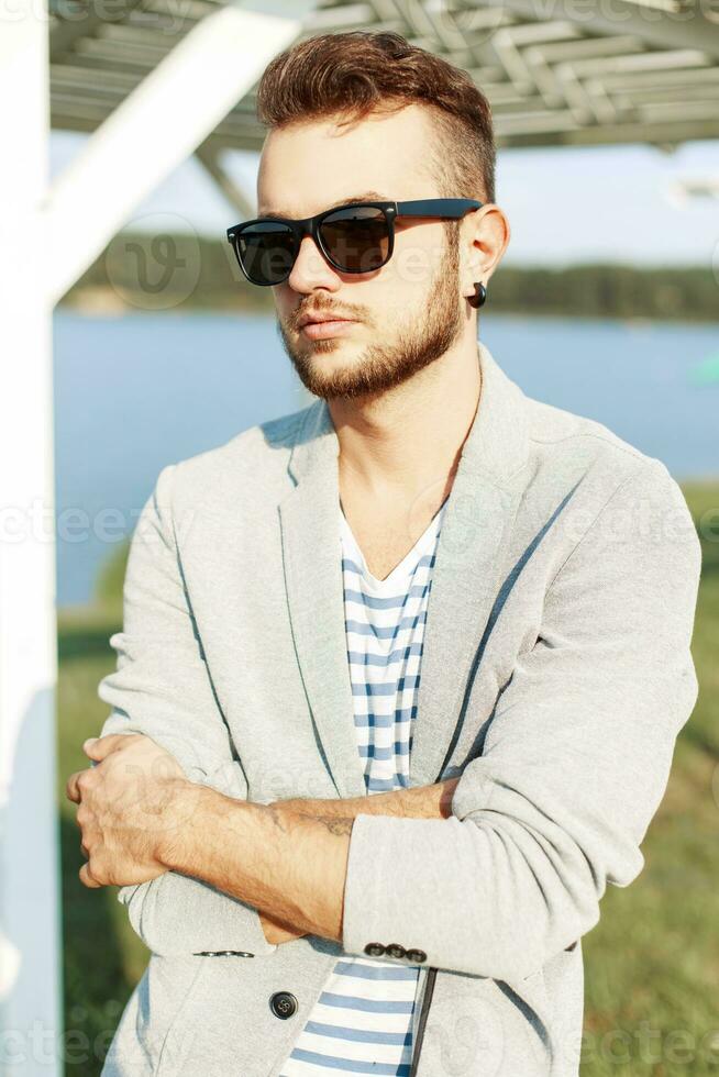 bello uomo con un' barba nel occhiali da sole e giacca su il spiaggia foto