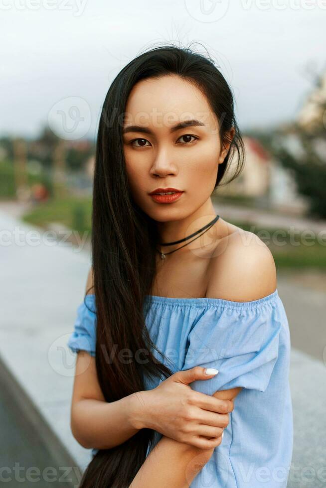 bellissimo giovane vietnamita ragazza con lungo acconciatura nel un' blu camicetta con spoglio le spalle su un' estate giorno foto