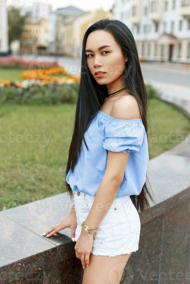 bellissimo giovane asiatico donna nel un' camicetta e pantaloncini a piedi nel il città. foto