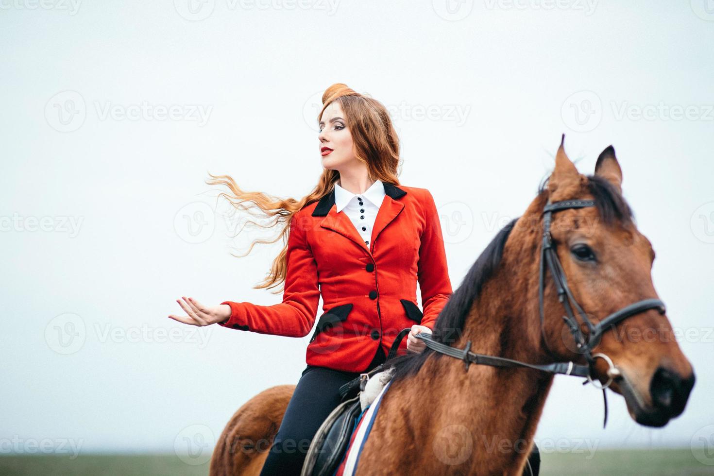 ragazza fantino dai capelli rossi in un cardigan rosso e stivali alti neri con un cavallo foto