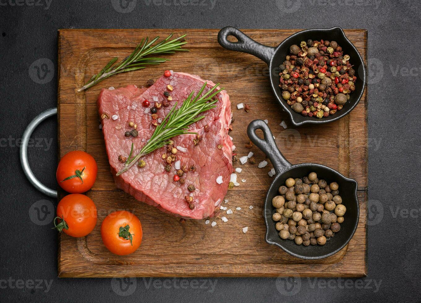 crudo pezzo di Manzo con spezie Pepe, rosmarino rametto, sale e oliva olio su un' di legno asse, nero sfondo foto