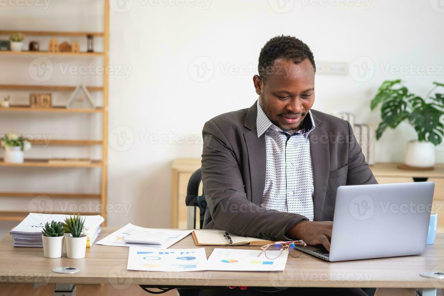 africano americano uomo d'affari analizzando il computer portatile grafico lavoro d'ufficio nel ufficio Tenere documenti preparazione portafoglio analisi rapporto nero maschio analista fare lavoro d'ufficio nel il posto di lavoro utilizzando il computer. foto