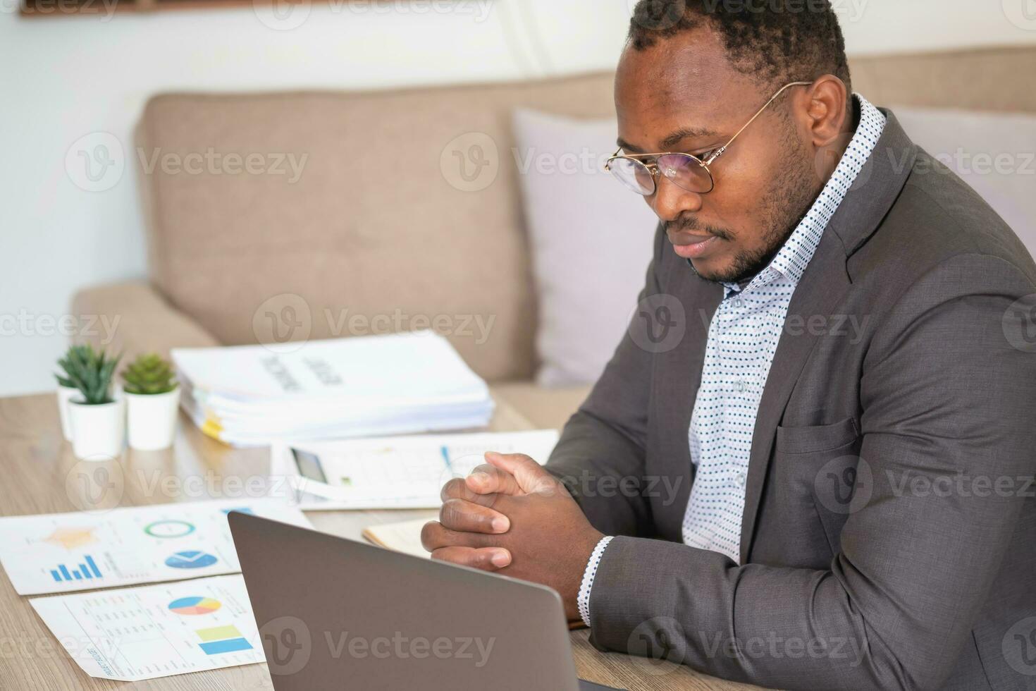 africano americano uomo d'affari analizzando il computer portatile grafico lavoro d'ufficio nel ufficio Tenere documenti preparazione portafoglio analisi rapporto nero maschio analista fare lavoro d'ufficio nel il posto di lavoro utilizzando il computer. foto