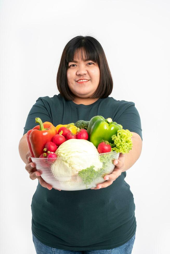 felice donna asiatica sovrappeso che tiene un cesto di verdure e sorridente su sfondo bianco isolato, il concetto di buona salute deriva dal mangiare una dieta nutriente. foto