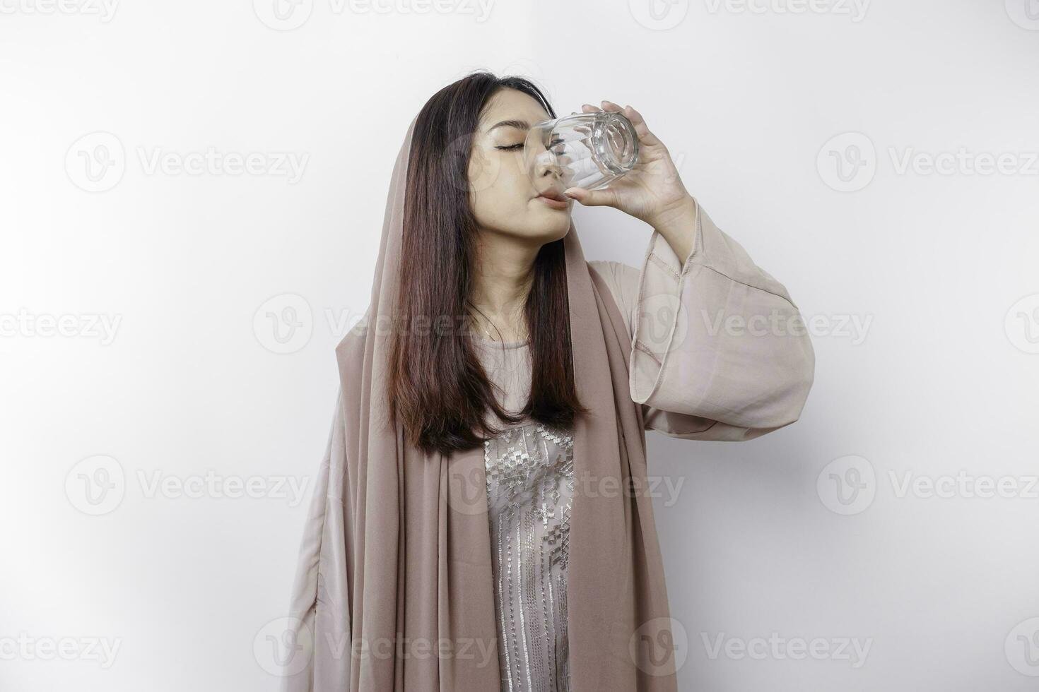 gioioso asiatico musulmano donna indossare foulard è potabile un' bicchiere di acqua, isolato su bianca sfondo. foto