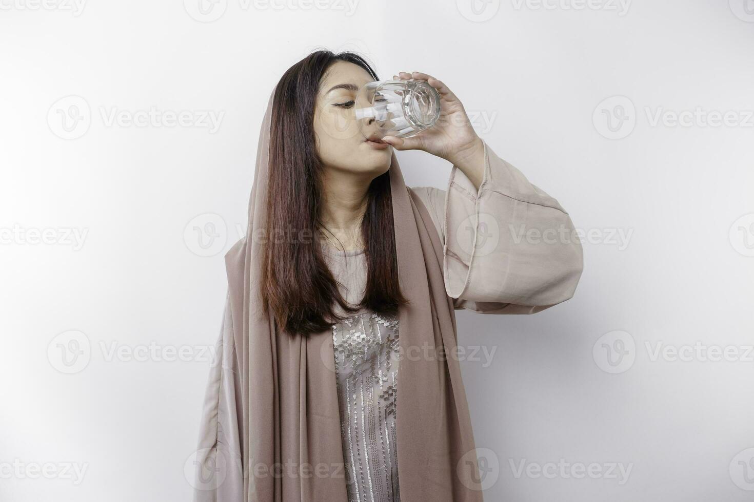 gioioso asiatico musulmano donna indossare foulard è potabile un' bicchiere di acqua, isolato su bianca sfondo. foto