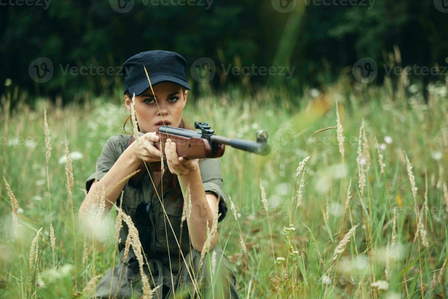 militare donna riparo si siede su il erba a caccia arma verde le foglie foto