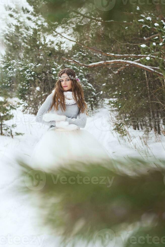 bellissimo sposa nel un' bianca vestito con un' mazzo nel un' innevato inverno foresta. ritratto di il sposa nel natura. foto