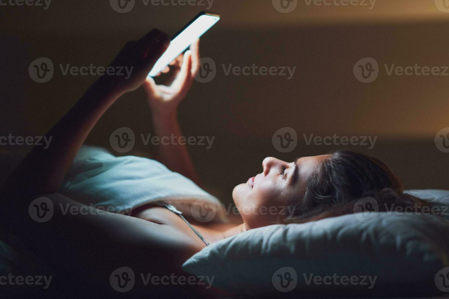 donna a notte nel letto con Telefono foto