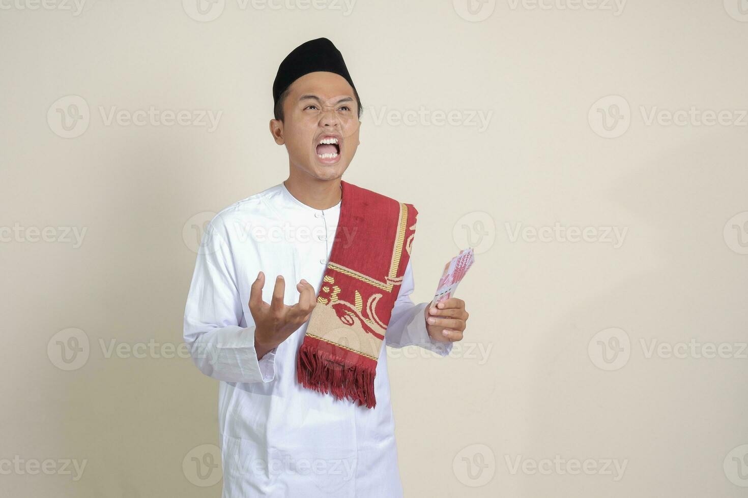 ritratto di attraente asiatico musulmano uomo nel bianca camicia fabbricazione arrabbiato gesto mostrando uno centinaio mille rupia. finanziario e risparmi concetto. isolato Immagine su grigio sfondo foto