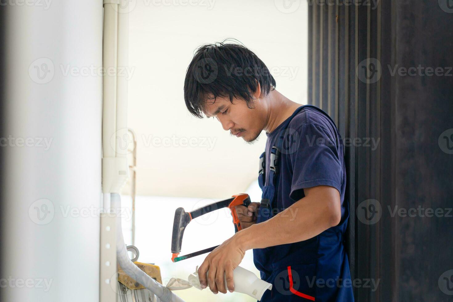 artigiano lavoratore segare un' tubo, tecnico uomo installazione un aria condizionata nel un' cliente Casa, giovane riparatore fissaggio aria condizionatore unità, Manutenzione e riparazione concetti foto