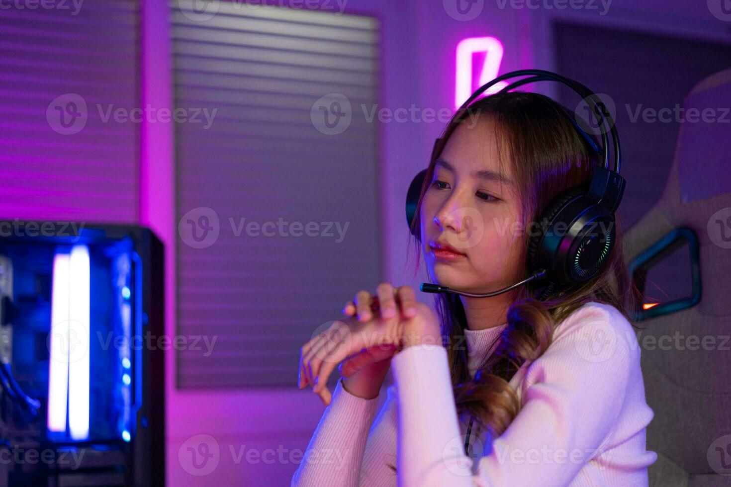 polso dolore concetto. gamer e e-sport in linea di asiatico donna giocando in linea computer video gioco con illuminazione effetto, trasmissione streaming vivere a casa. sua uso sua polso per un' lungo volta. foto