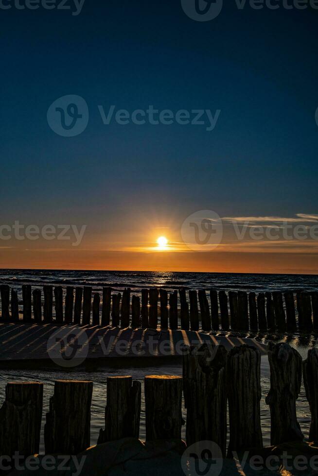 colorato tramonto al di sopra di il polacco baltico mare con buio cielo nuvole e frangiflutti foto