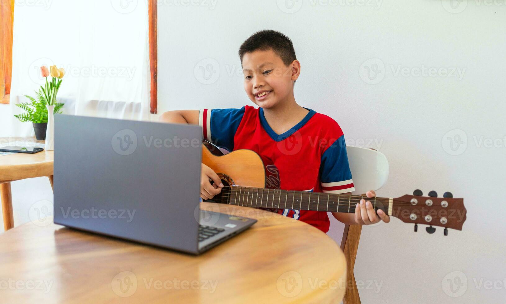 il storia di un' ragazzo Guardando un' taccuino computer mentre preparazione per pratica giocando chitarra a casa. ragazzi prendere classico chitarra Lezioni in linea. foto