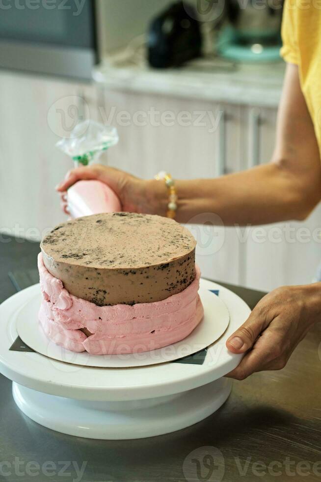 donna fabbricazione cioccolato torta con rosa crema, avvicinamento. torta fabbricazione processi, selettivo messa a fuoco foto