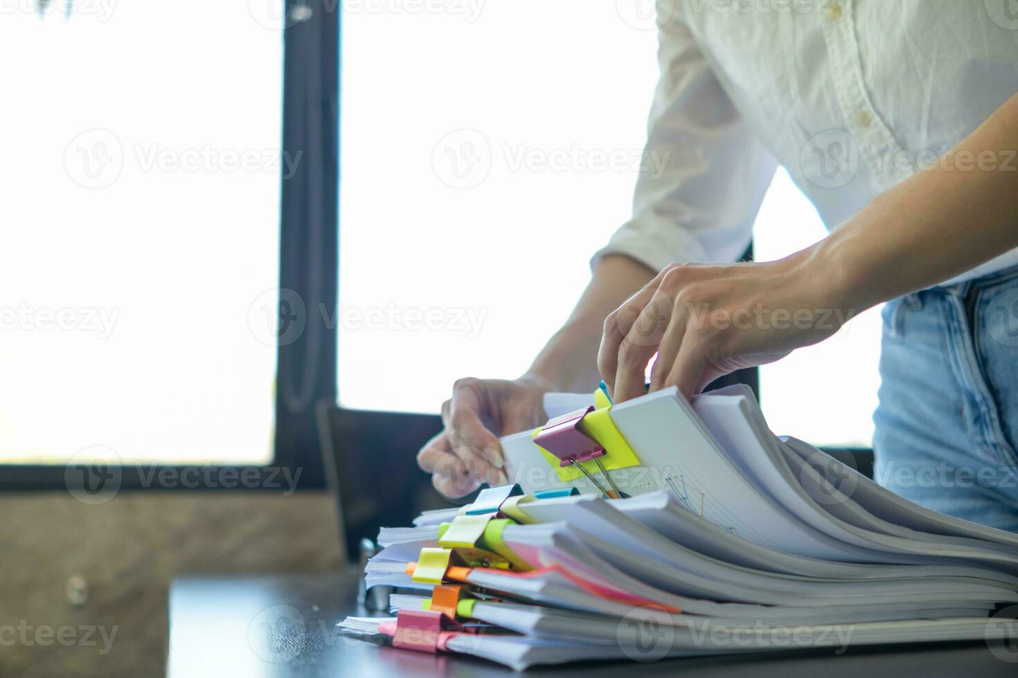 donna d'affari mani Lavorando su pile di carta documenti per ricerca e revisione documenti ammucchiati su tavolo prima invio loro per tavola di registi per uso corretta documenti nel incontro con uomo d'affari foto