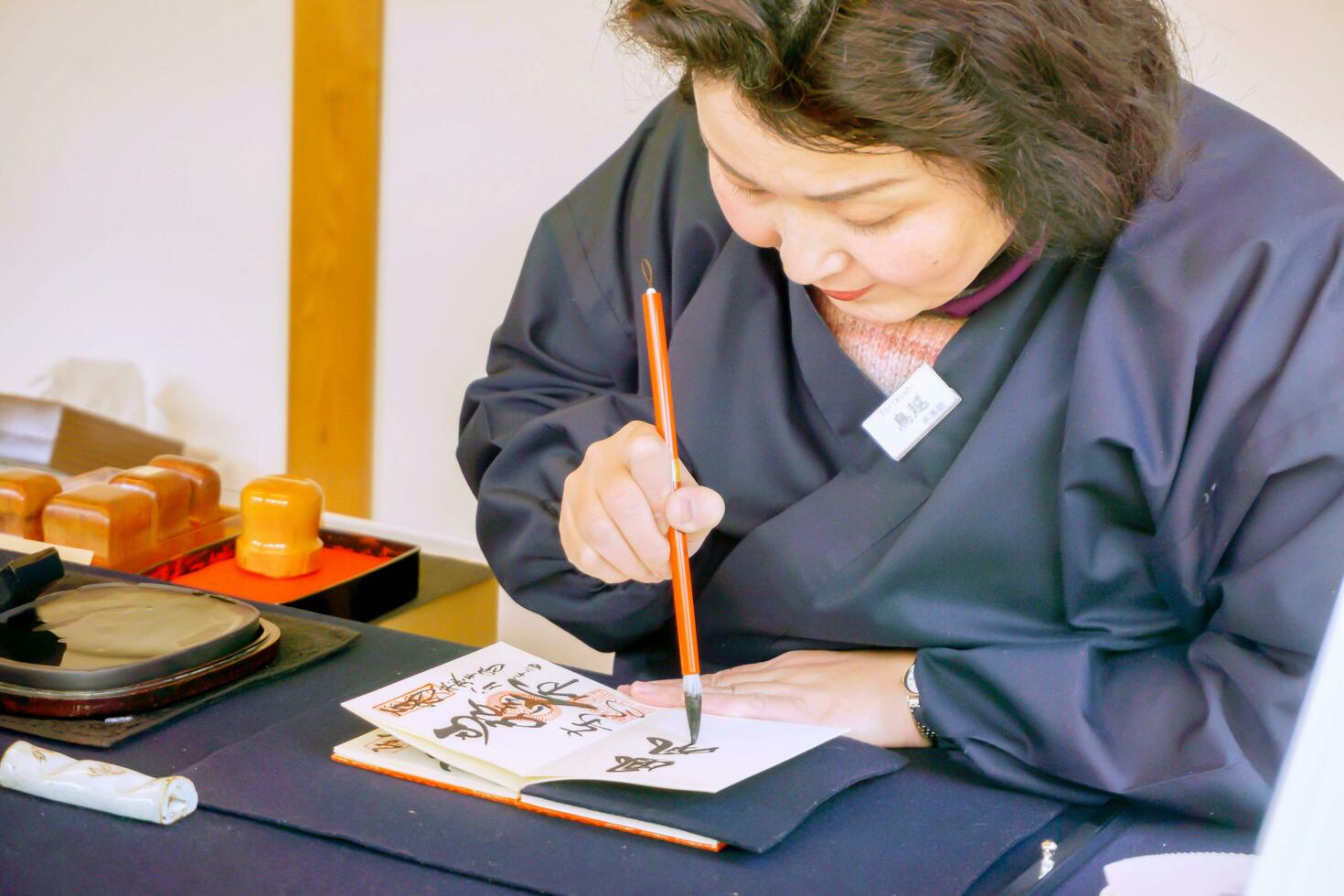 uji, kyoto prefettura, Giappone, 2018 - giapponese donne indossare un' blu nazionale vestito e Tenere un' Cinese spazzola scrittura giapponese testi a partire dal nero inchiostro su un' taccuino carta. foto
