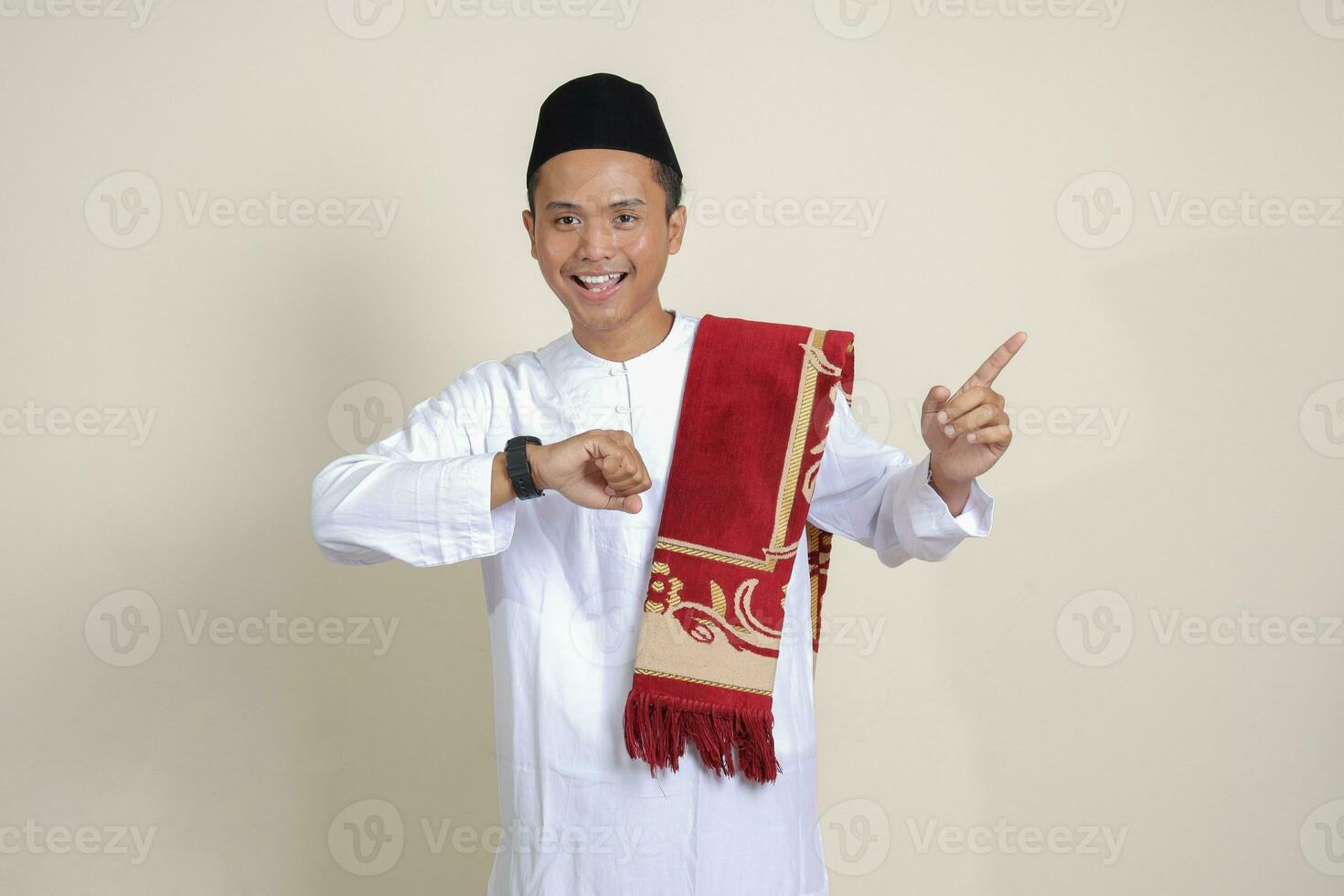 ritratto di attraente asiatico musulmano uomo nel bianca camicia guardare su polso orologio whille puntamento lontano con il suo dito. isolato Immagine su grigio sfondo foto