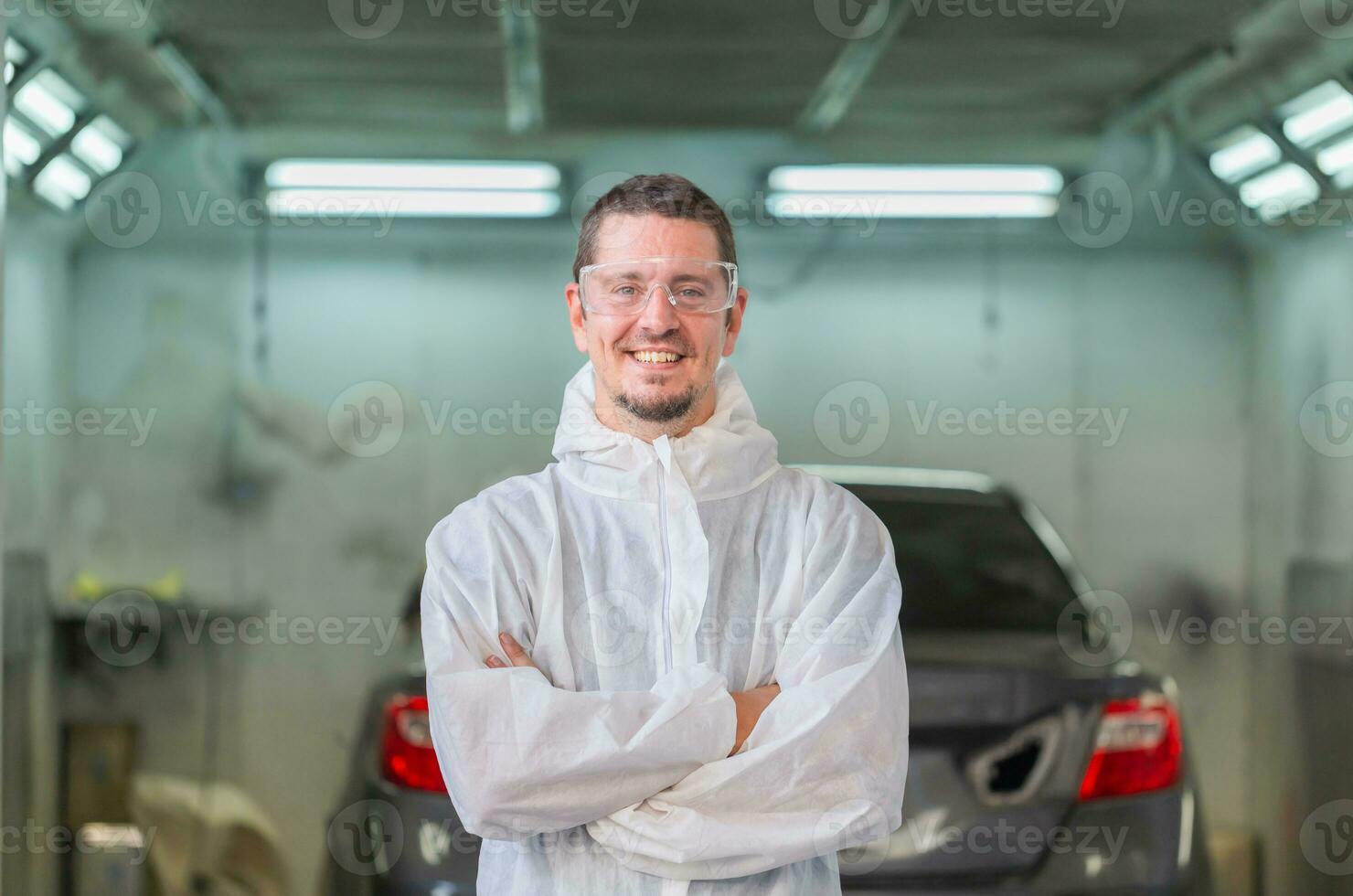 meccanico pittura auto in piedi con braccia attraversato nel Camera, allegro lavoratore uomo nel un' riparazione box auto, box auto pittura auto servizio riparazione e Manutenzione foto