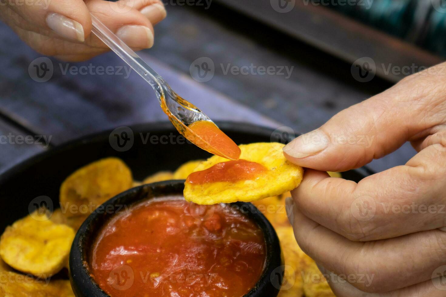 avvicinamento di donna di mani mentre mangiare piantaggine patatine fritte servito con colombiano tradizionale hogao foto