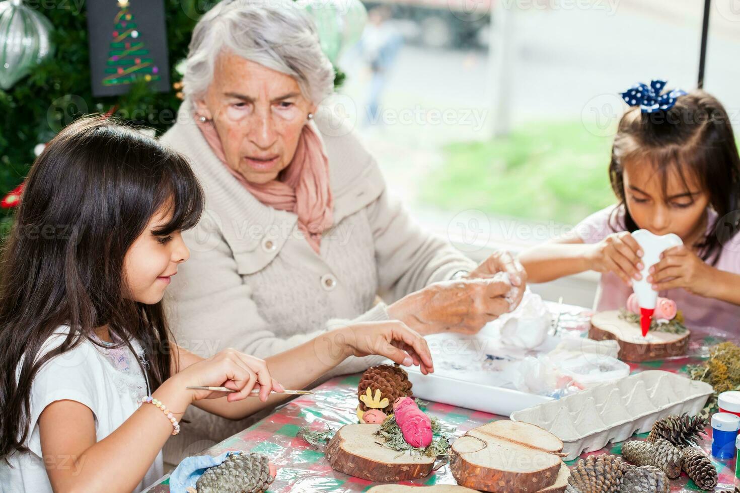 poco ragazza avendo divertimento con sua sorella e loro nonna mentre fabbricazione Natale Natività mestieri - vero famiglia foto