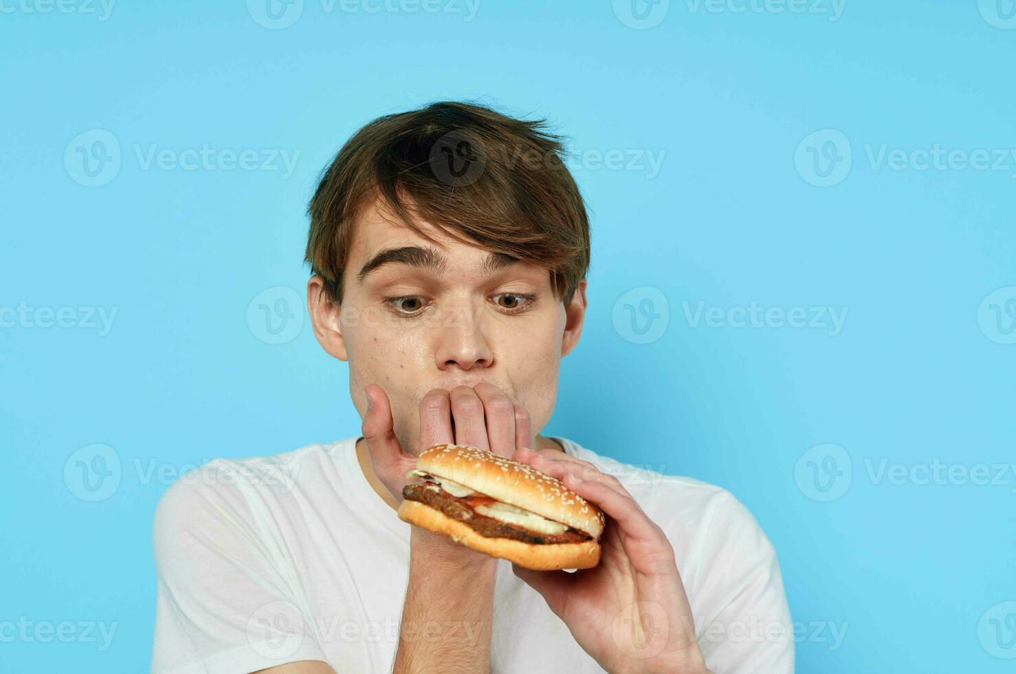 un' uomo nel un' bianca maglietta Hamburger mangiare un' merenda cibo foto