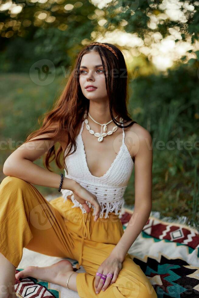 giovane bellissimo hippie donna seduta su il terra nel natura nel il autunno nel eco capi di abbigliamento nel il tramonto luce, un' stile di vita di viaggio e armonia con il mondo foto