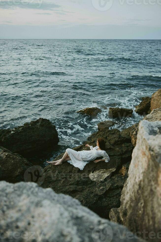 bellissimo sposa nel lungo bianca vestito bagnato capelli dire bugie su un' roccioso scogliera vacanza concetto foto