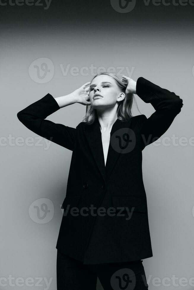 un elegante elegante ragazza pieghe sua capelli dietro a sua orecchie e solleva sua mani su. un' elegante signora nel un' completo da uomo pose nel il studio. il concetto di stile per Marche foto