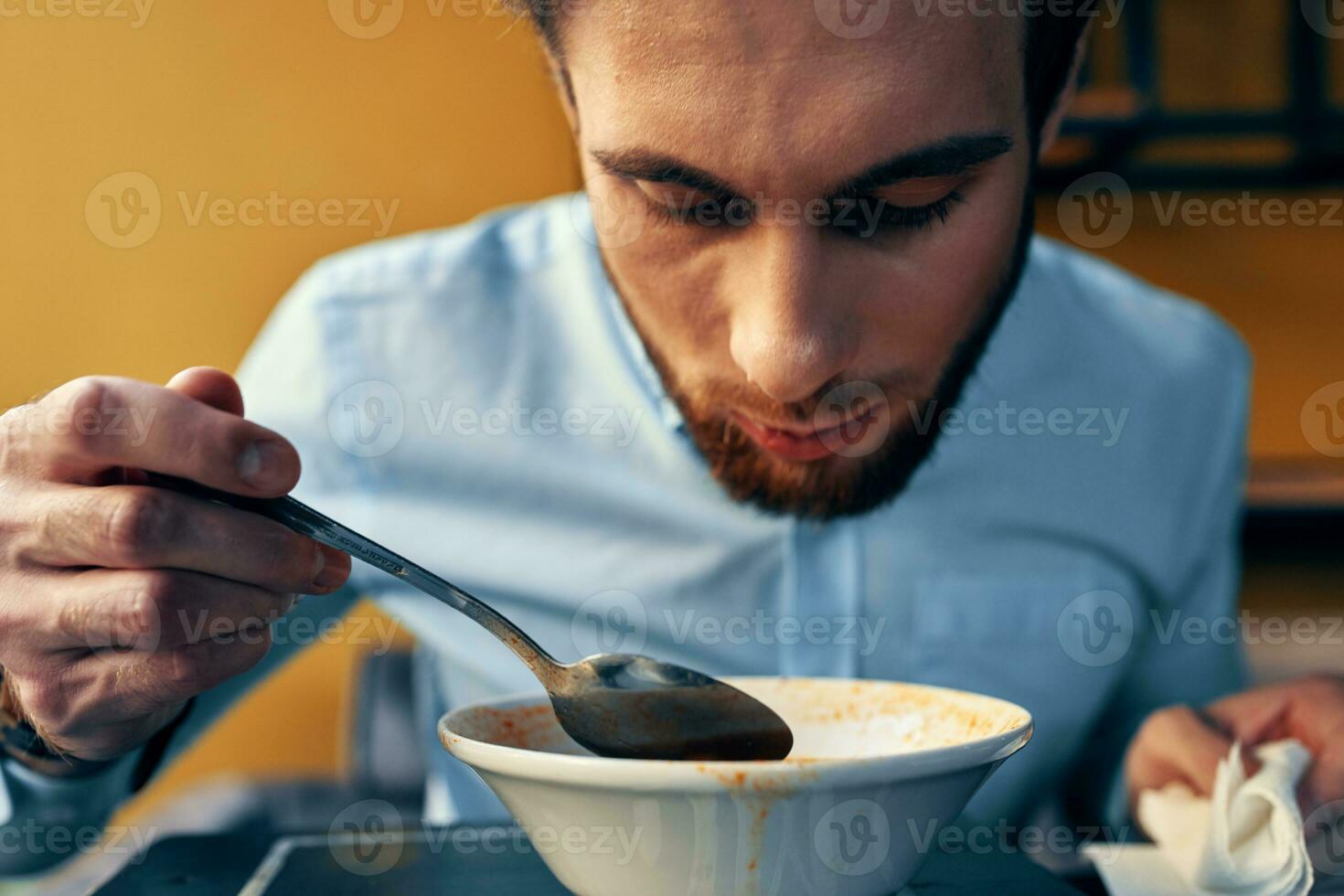 un' bello uomo con un' barba mangia borscht nel un' piatto a un' tavolo nel un' bar e un' orologio su il suo mano foto