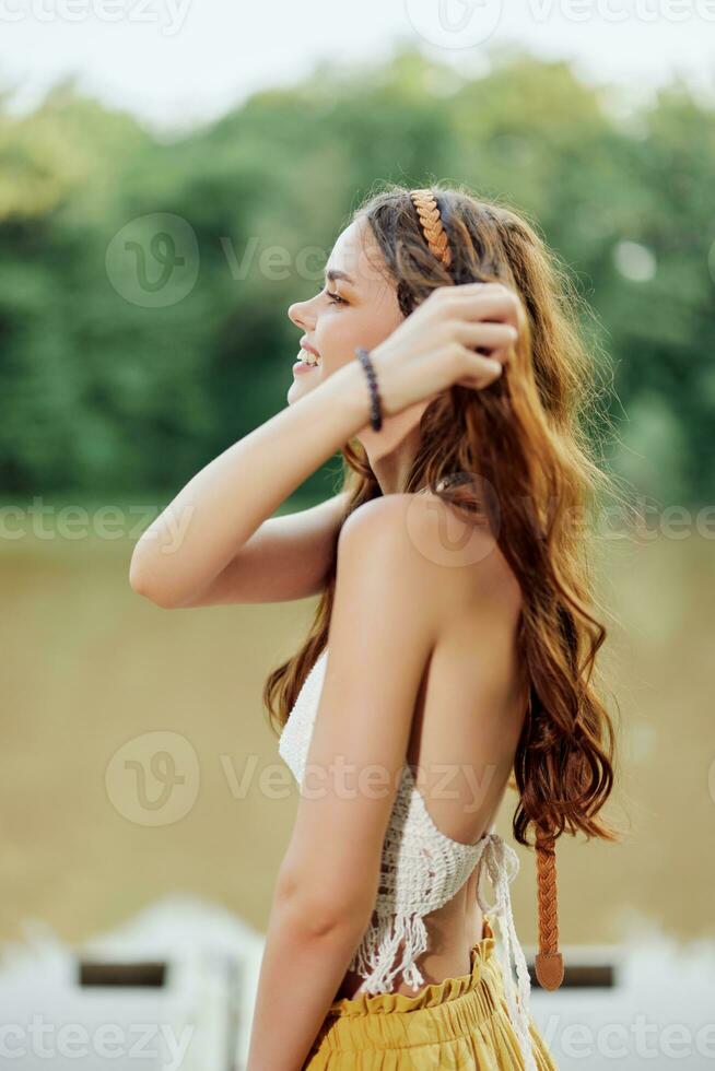 un' giovane donna sorridente nel un Immagine di un' hippie e eco-abito danza nel natura di il lago indossare un' cappello e giallo pantaloni nel il estate tramonto foto