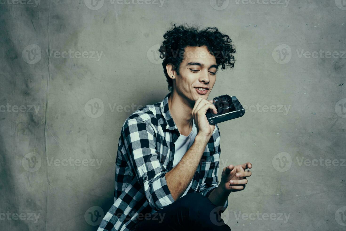 tipo con un' telecamera nel il suo mani su un' grigio sfondo in casa passatempo plaid camicia modello foto