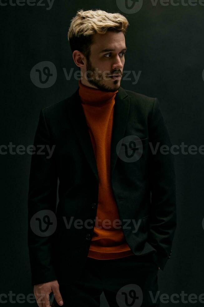 elegante uomo con un' alla moda acconciatura e nel un' pelle giacca arancia maglione nero sfondo foto