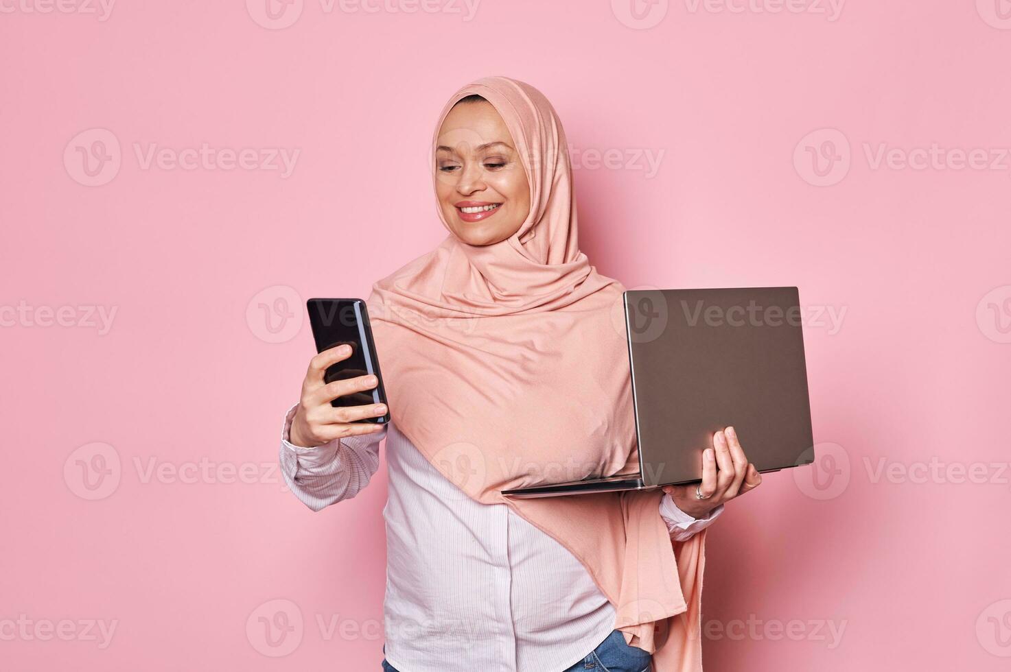 arabo musulmano donna, Lavorando incinta attività commerciale signora nel rosa hijab, con mobile Telefono e il computer portatile. gravidanza e carriera foto