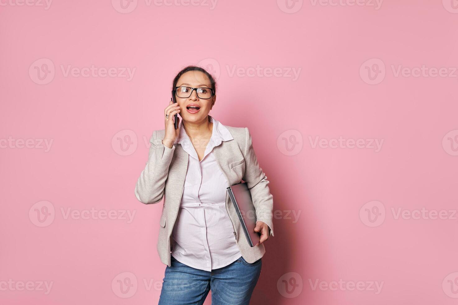 elegante incinta donna parlando su mobile Telefono, negoziazione con attività commerciale partner, concludere offerte su rosa sfondo foto