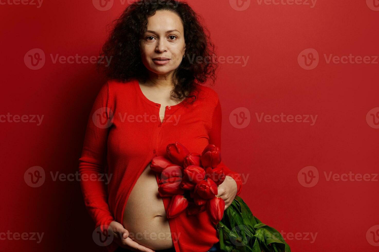 autentico studio ritratto bellissimo incinta donna, in attesa madre in posa con mazzo di tulipani su rosso colore sfondo foto