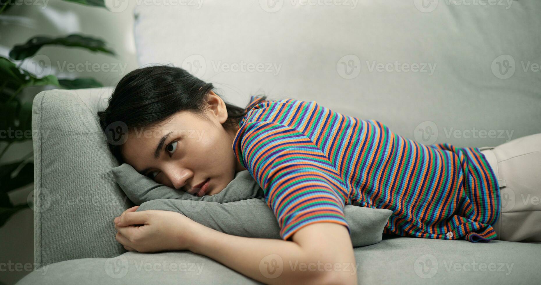 pigro giovane asiatico femmina dire bugie su un' confortevole divano nel il vivente camera a casa foto