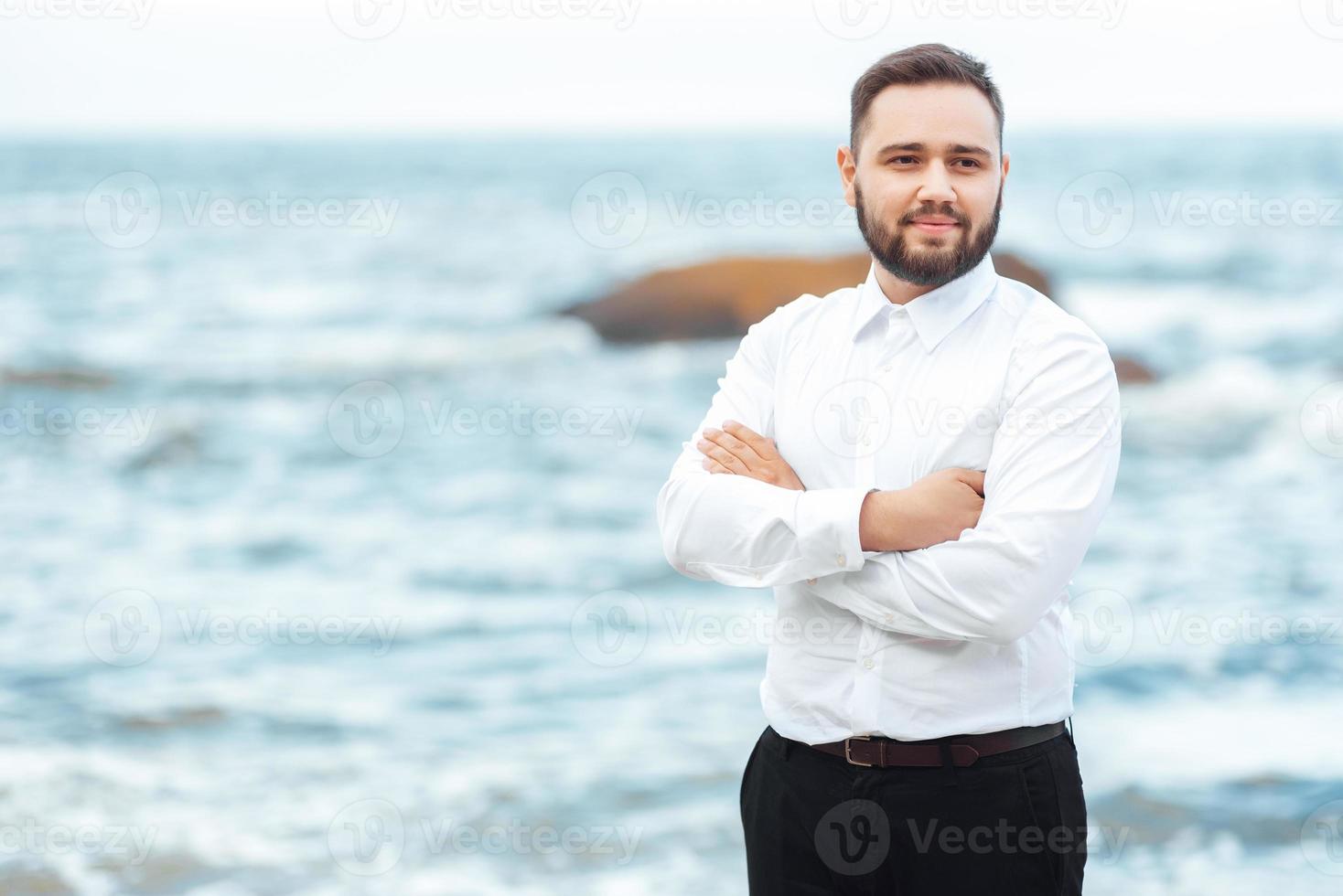 sposo in camicia bianca e pantaloni neri in riva al mare foto