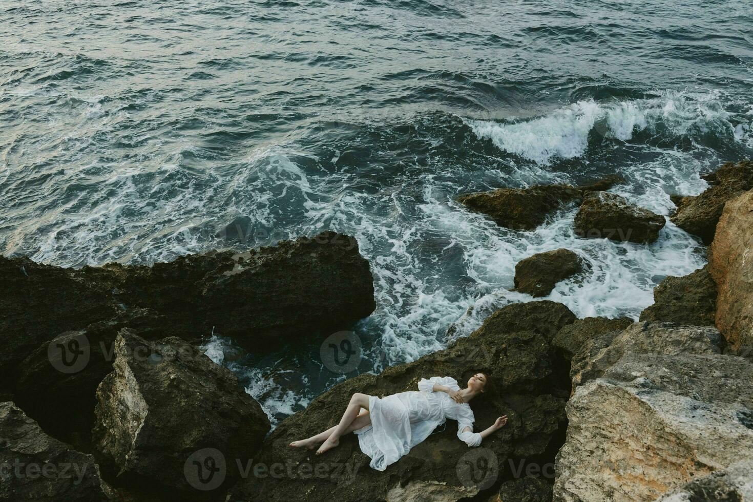 bellissimo donna nel lungo bianca vestito bagnato capelli dire bugie su un' roccioso scogliera inalterato foto