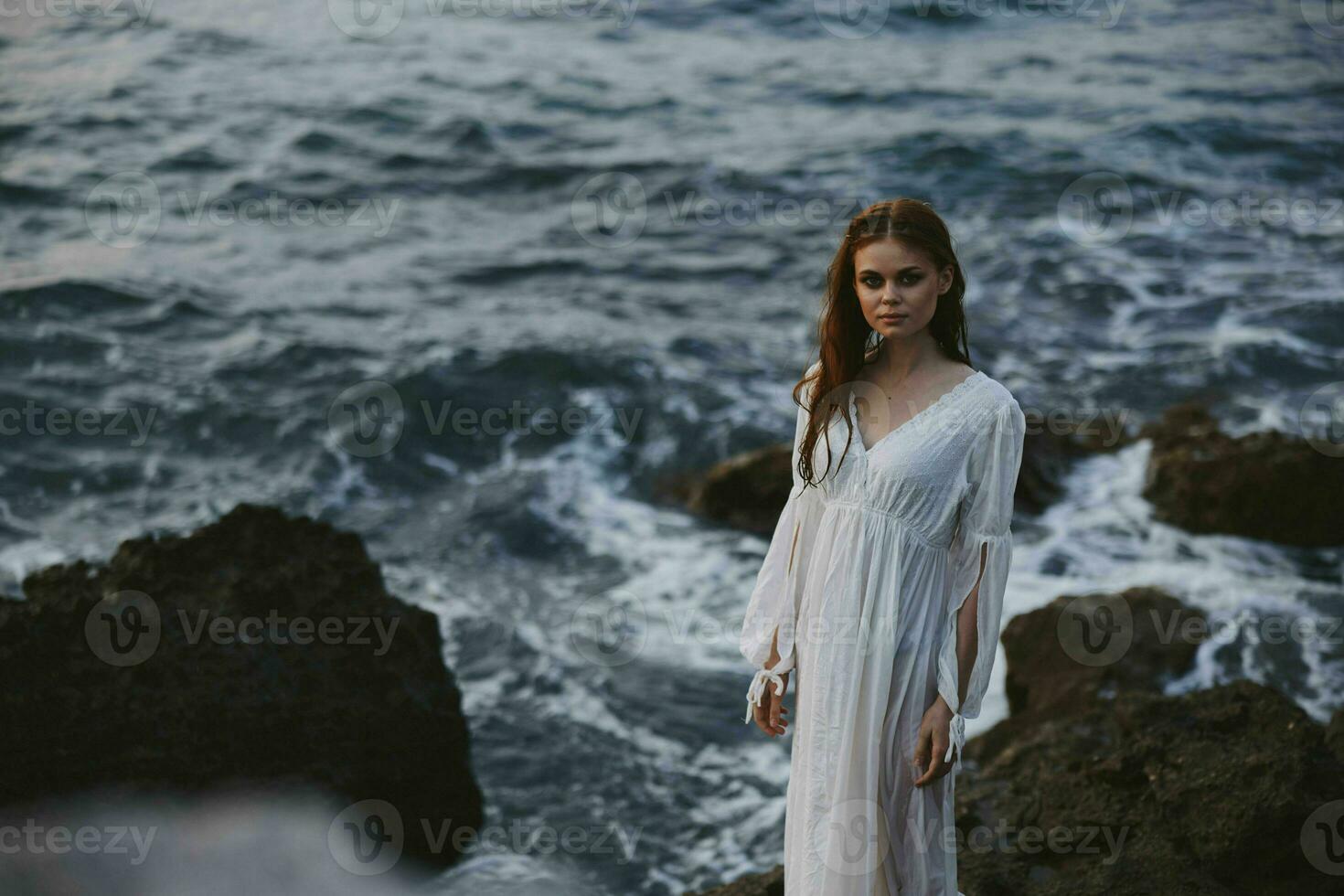 un' donna nel un' bianca vestito sta su il riva di il oceano pietre viaggio inalterato foto