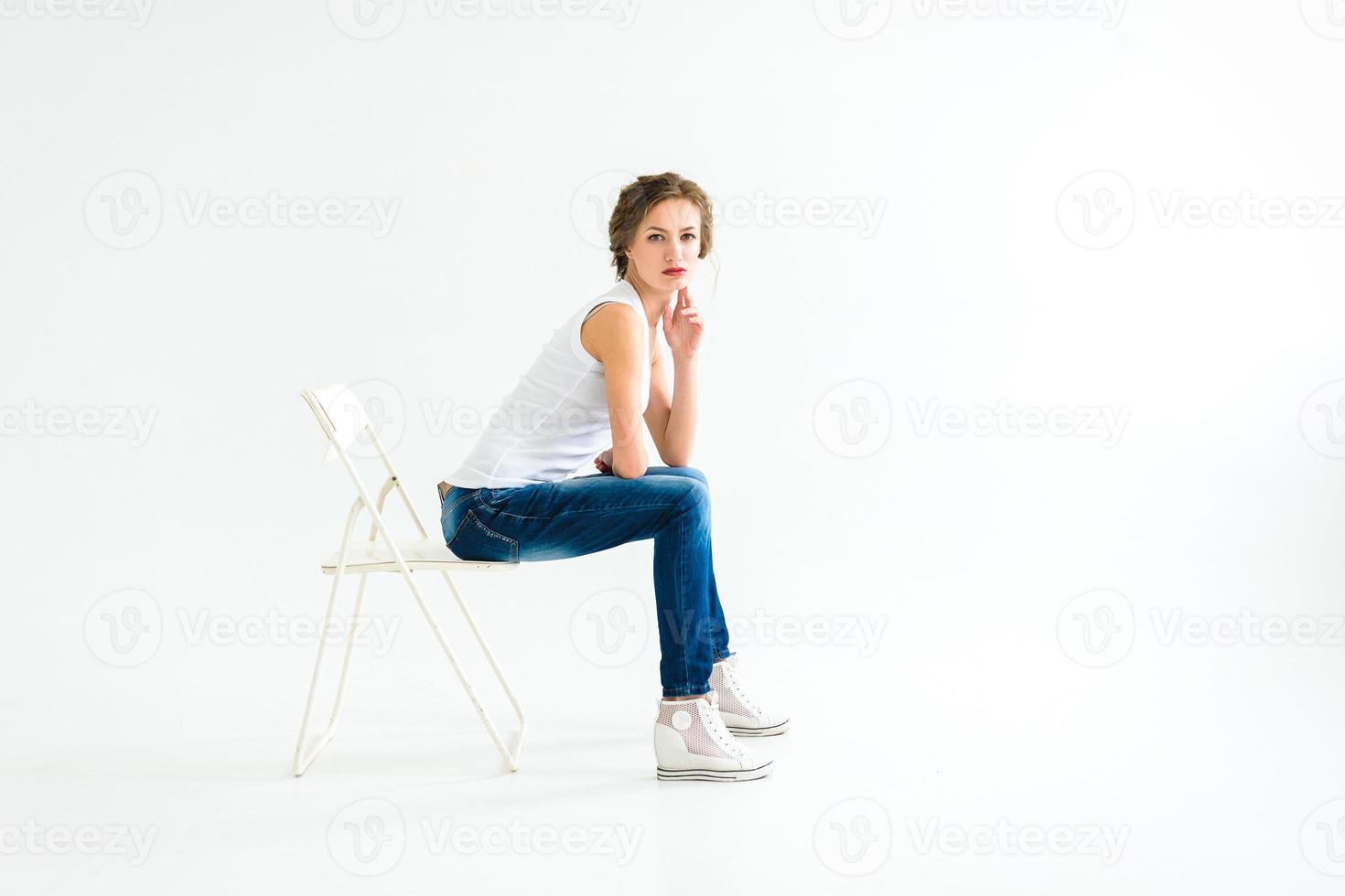 ragazza allegra in una maglietta bianca e jeans blu scuro in studio su sfondo bianco foto