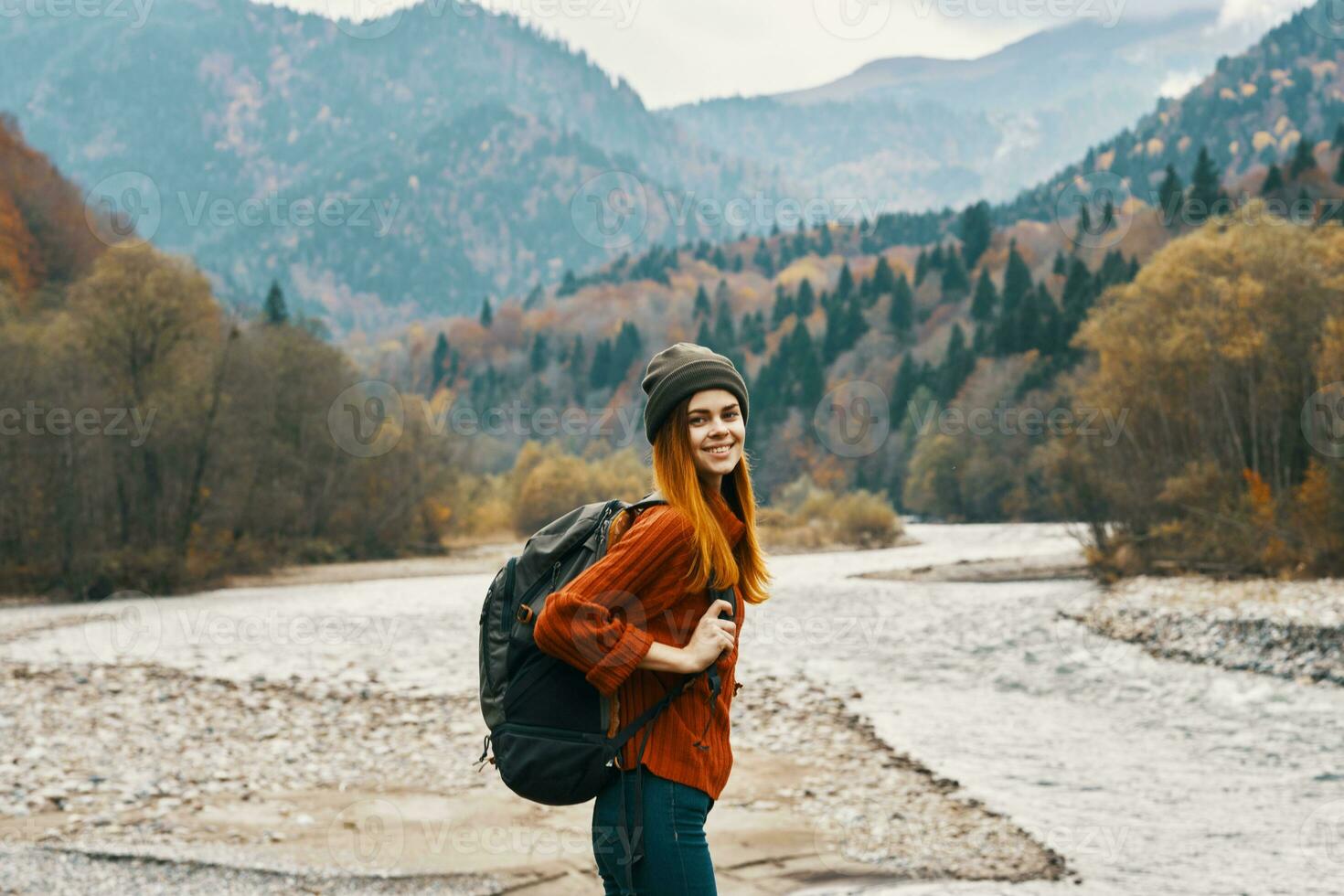 gioioso donna turista con un' zaino sembra a il montagne vicino il fiume su il banca foto